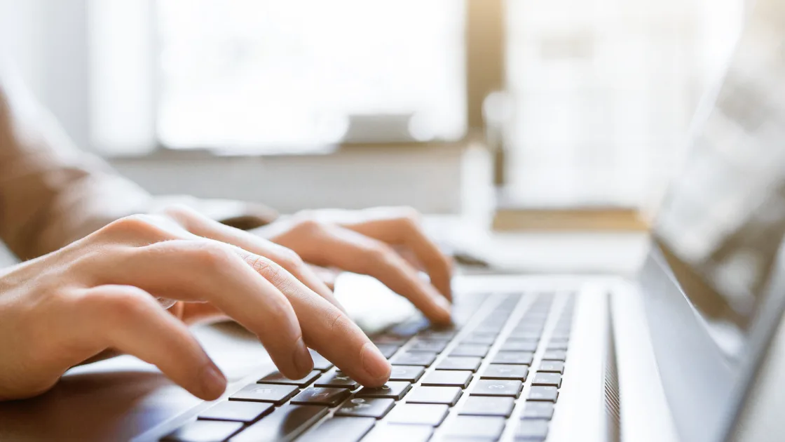 Hands typing on a laptop keyboard in a bright home office